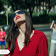A woman wearing a red top and sunglasses looks to the sky